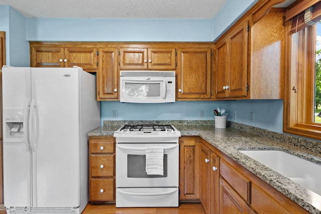 kitchen featuring light stone counters, white appliances, and brown cabinets