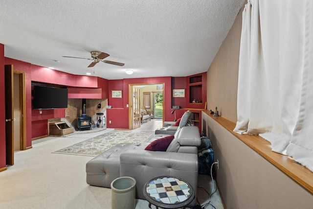 carpeted living area featuring a textured ceiling, a wood stove, and a ceiling fan