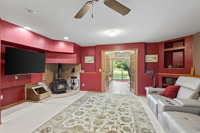 carpeted living area featuring a wood stove, a ceiling fan, baseboards, and a textured ceiling