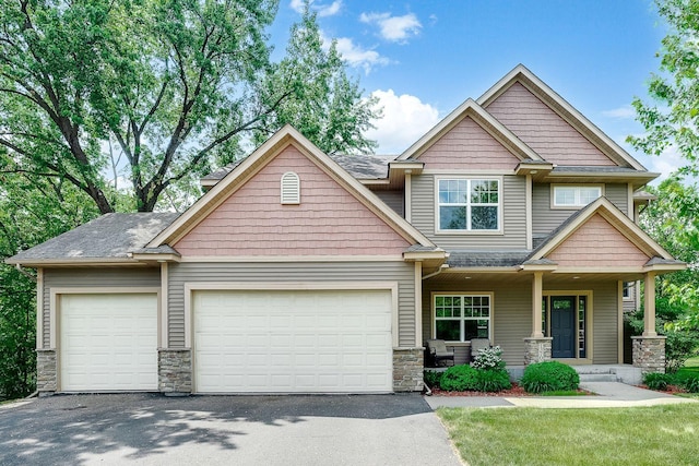 craftsman-style home featuring driveway, an attached garage, covered porch, and stone siding