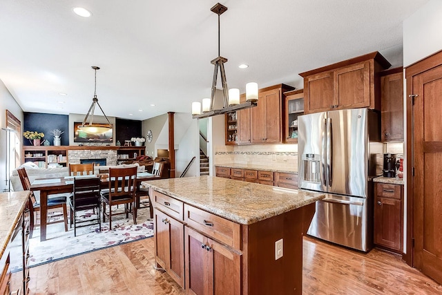 kitchen with brown cabinets, decorative light fixtures, stainless steel fridge, light wood finished floors, and decorative backsplash