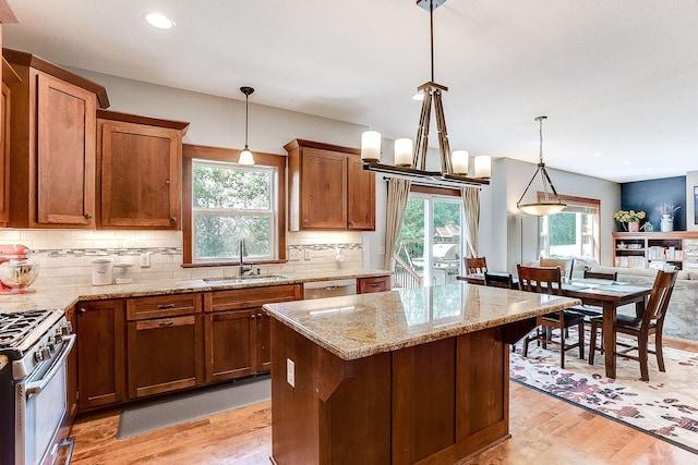 kitchen with light stone countertops, light wood-type flooring, brown cabinetry, stainless steel appliances, and a sink