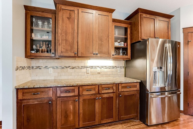 kitchen featuring decorative backsplash, glass insert cabinets, light stone counters, and stainless steel fridge with ice dispenser