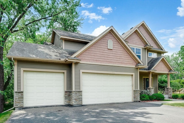 craftsman-style home featuring an attached garage, stone siding, driveway, and a shingled roof