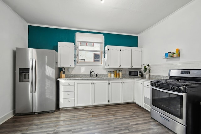 kitchen with crown molding, appliances with stainless steel finishes, wood finished floors, white cabinets, and a sink