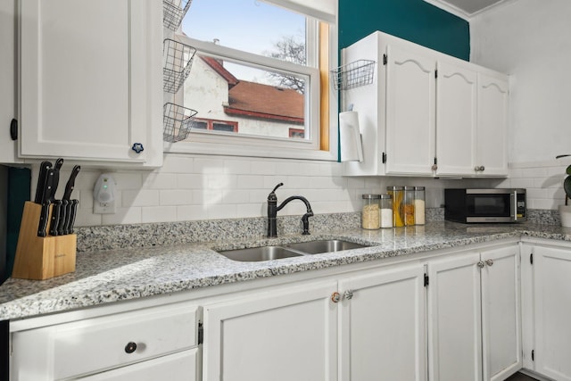 kitchen featuring tasteful backsplash, stainless steel microwave, light stone countertops, white cabinetry, and a sink