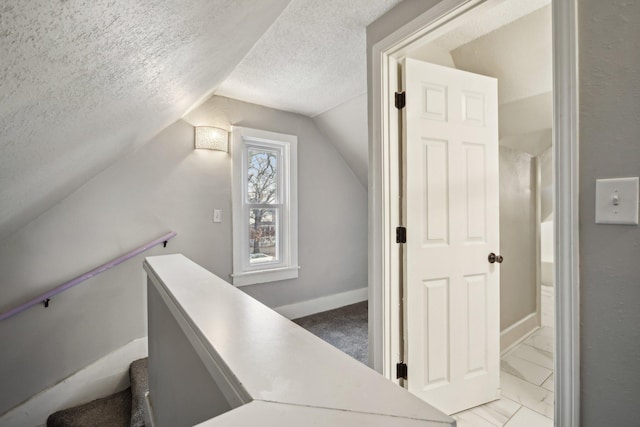 stairway featuring baseboards, lofted ceiling, and a textured ceiling