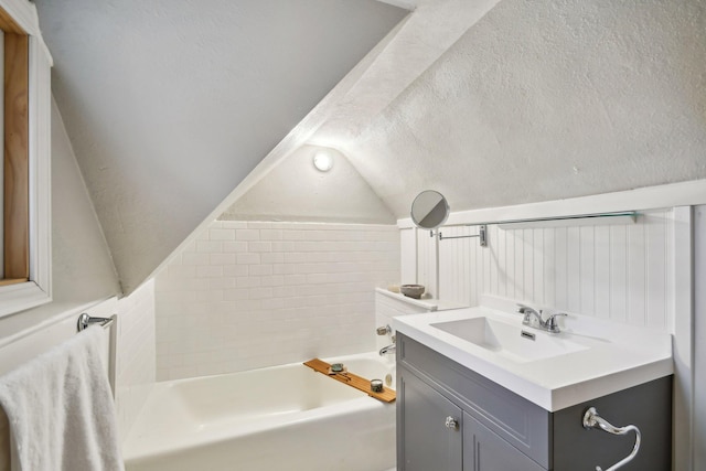 full bathroom with a textured ceiling, a tub, vanity, and vaulted ceiling