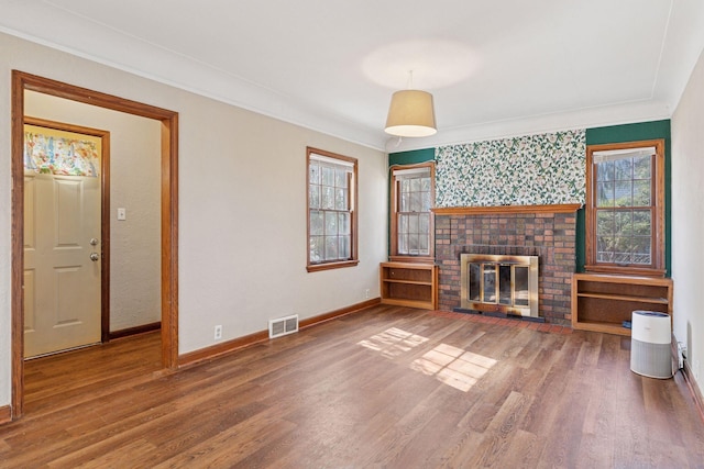 unfurnished living room featuring wood finished floors, visible vents, baseboards, a fireplace, and crown molding