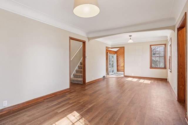 empty room featuring stairway, baseboards, wood finished floors, and crown molding