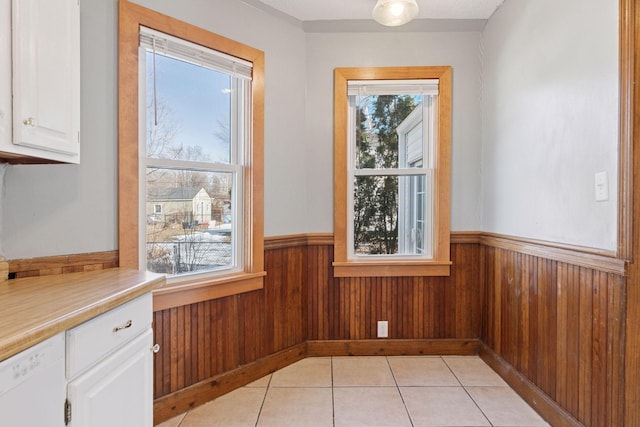 unfurnished dining area with light tile patterned flooring, a wainscoted wall, and wood walls