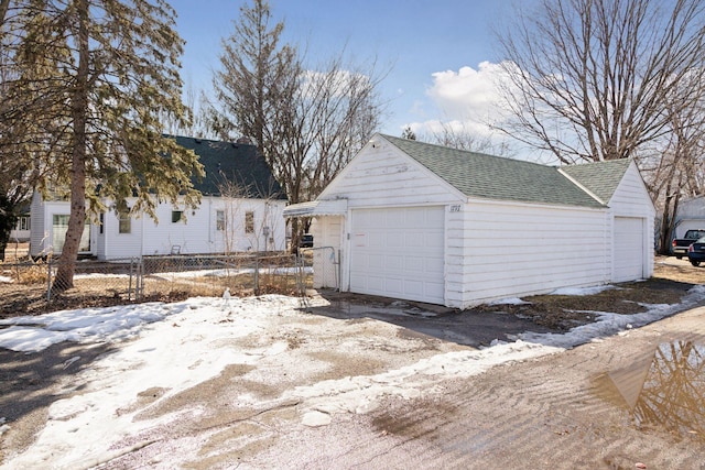 snow covered garage with a detached garage and fence