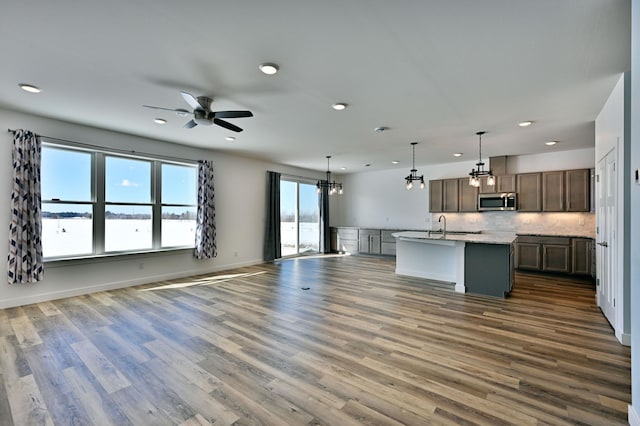 kitchen featuring a kitchen island with sink, decorative backsplash, dark wood-type flooring, stainless steel microwave, and open floor plan