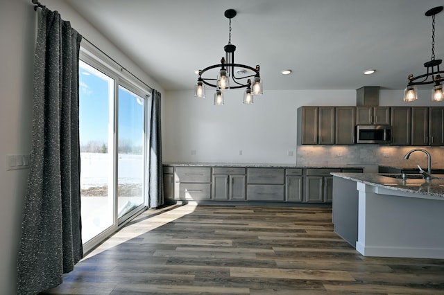 kitchen with a sink, stainless steel microwave, tasteful backsplash, dark wood finished floors, and a chandelier