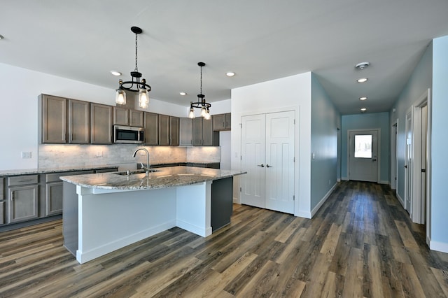 kitchen with stainless steel microwave, stone countertops, decorative backsplash, and a sink