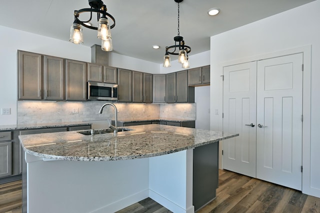 kitchen featuring light stone countertops, dark wood finished floors, a sink, stainless steel microwave, and backsplash