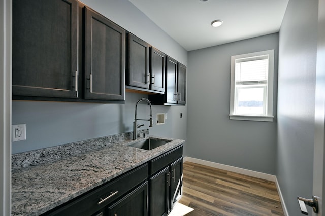 kitchen featuring dark wood finished floors, light stone counters, baseboards, and a sink