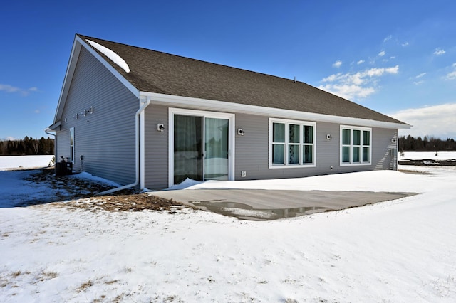 snow covered back of property featuring central air condition unit and a shingled roof