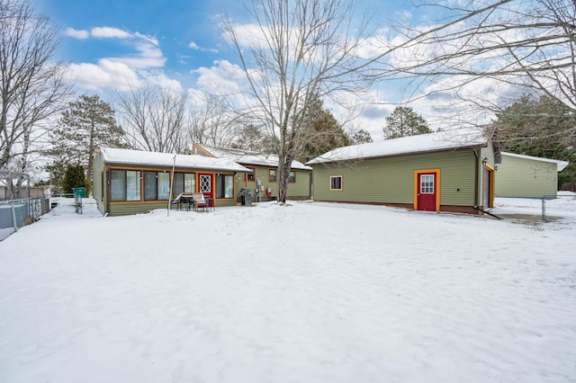 snow covered house featuring a sunroom and fence