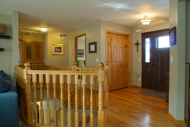 foyer entrance featuring a textured ceiling, baseboards, visible vents, and light wood-type flooring