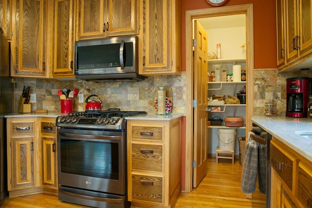 kitchen featuring light wood-type flooring, brown cabinets, stainless steel appliances, light countertops, and decorative backsplash