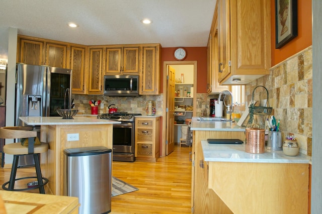 kitchen with light countertops, a kitchen breakfast bar, light wood-style floors, stainless steel appliances, and a sink