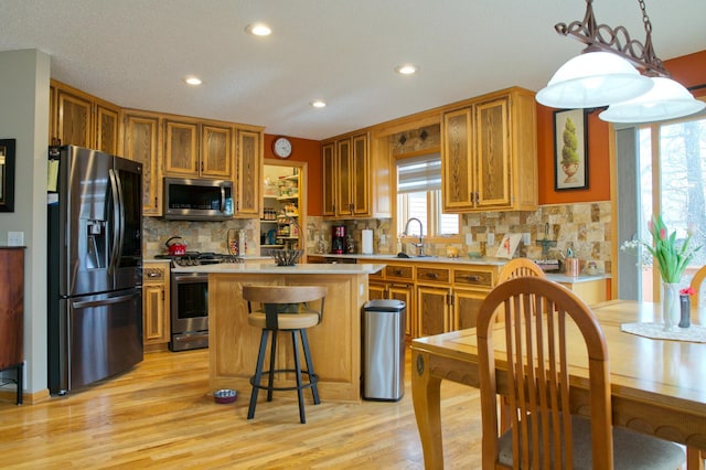 kitchen with a sink, a center island, stainless steel appliances, brown cabinetry, and light countertops