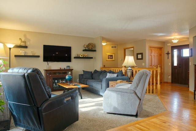 living area featuring visible vents, light wood-style floors, and a glass covered fireplace