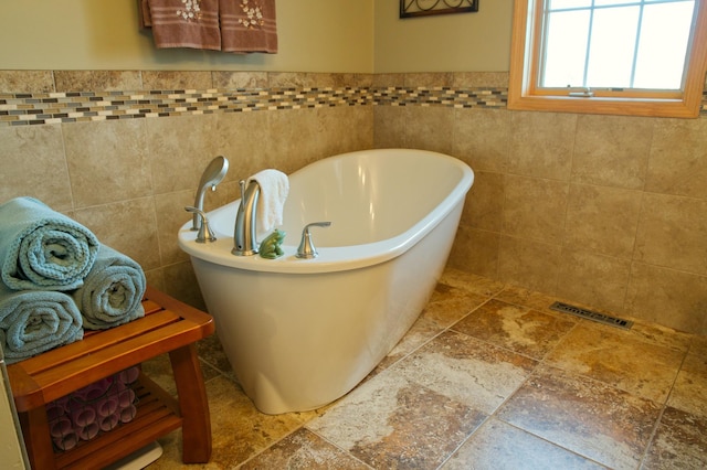 bathroom featuring visible vents, a soaking tub, tile walls, and stone tile floors