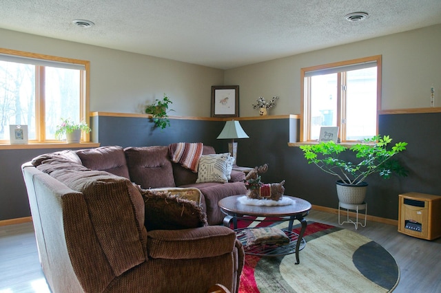 living area with visible vents, baseboards, a textured ceiling, and wood finished floors