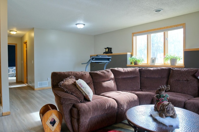 living room featuring baseboards, visible vents, a textured ceiling, and light wood-style floors