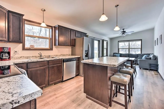 kitchen with a sink, a kitchen breakfast bar, stainless steel dishwasher, light wood finished floors, and dark brown cabinets