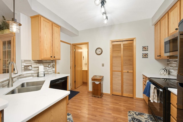 kitchen with a sink, black appliances, light countertops, tasteful backsplash, and light wood-type flooring