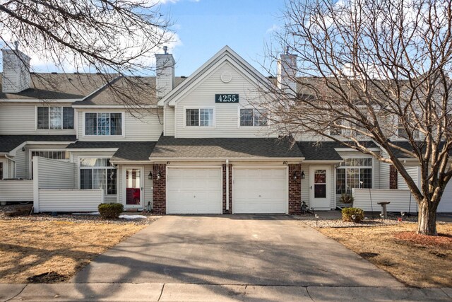 view of front of house with concrete driveway, roof with shingles, an attached garage, brick siding, and a chimney