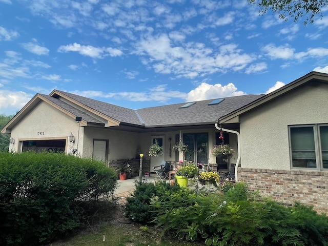 exterior space with stucco siding, a garage, roof with shingles, and brick siding