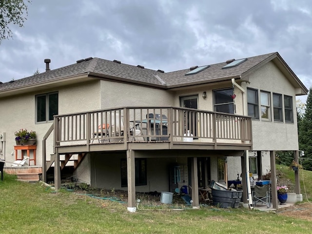 rear view of property featuring stucco siding, a wooden deck, a yard, and roof with shingles