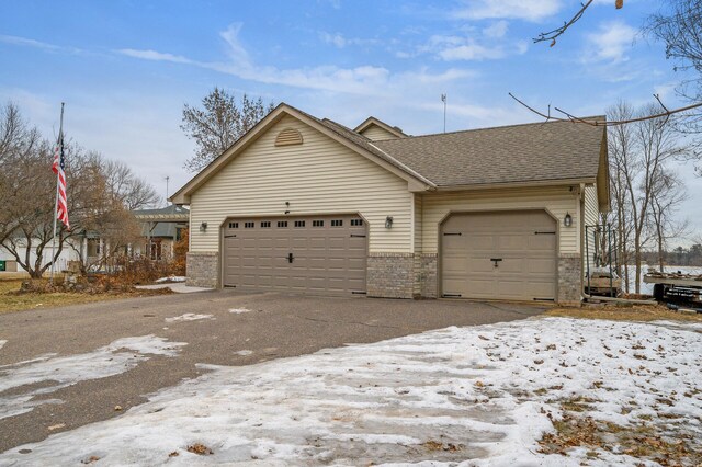 view of front of house with brick siding, a garage, and roof with shingles