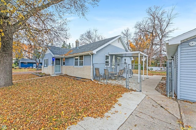 view of front of house featuring brick siding, a shingled roof, fence, a chimney, and a gate