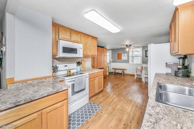 kitchen with white appliances, a ceiling fan, light wood finished floors, a sink, and a textured ceiling