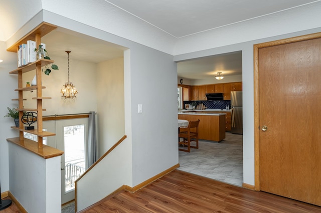 corridor with an upstairs landing, a chandelier, light wood finished floors, and baseboards