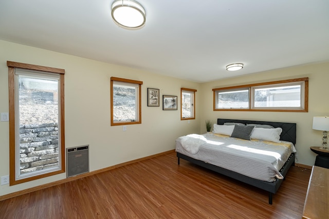 bedroom with baseboards, heating unit, and wood finished floors