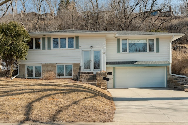 raised ranch featuring french doors, concrete driveway, an attached garage, and a front yard