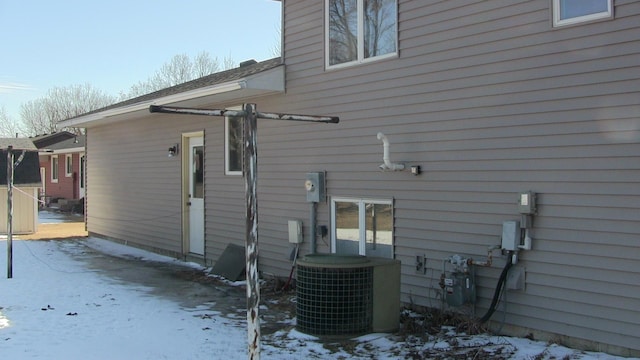 snow covered back of property featuring central AC