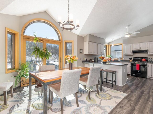 dining area featuring ceiling fan with notable chandelier, vaulted ceiling, and dark wood-style floors