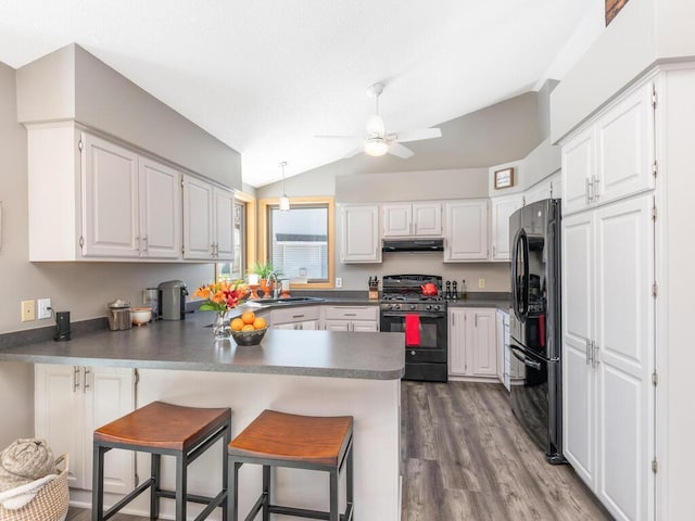 kitchen featuring a peninsula, a sink, black appliances, under cabinet range hood, and dark countertops