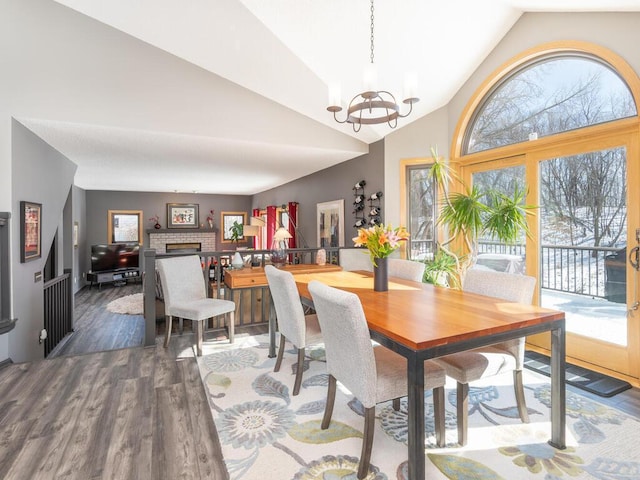 dining area featuring an inviting chandelier, wood finished floors, a fireplace, and vaulted ceiling