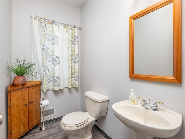 half bath featuring visible vents, toilet, wood finished floors, and a sink