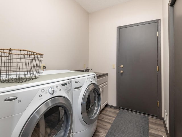 laundry room featuring a sink, wood finished floors, cabinet space, and washer and clothes dryer