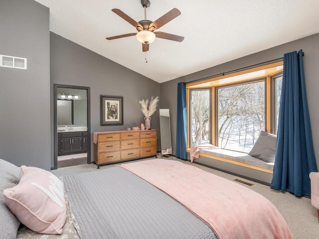 bedroom featuring visible vents, light colored carpet, lofted ceiling, ensuite bath, and a sink