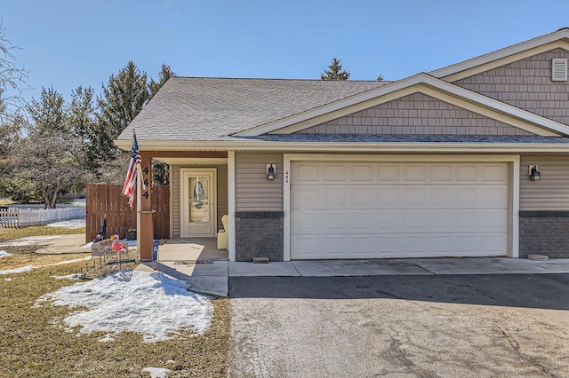 view of front facade with aphalt driveway, a garage, roof with shingles, and fence